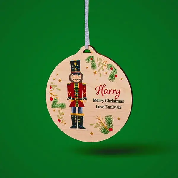 Personalised wooden Christmas bauble featuring a nutcracker illustration, festive foliage, and custom Christmas message on a green background.